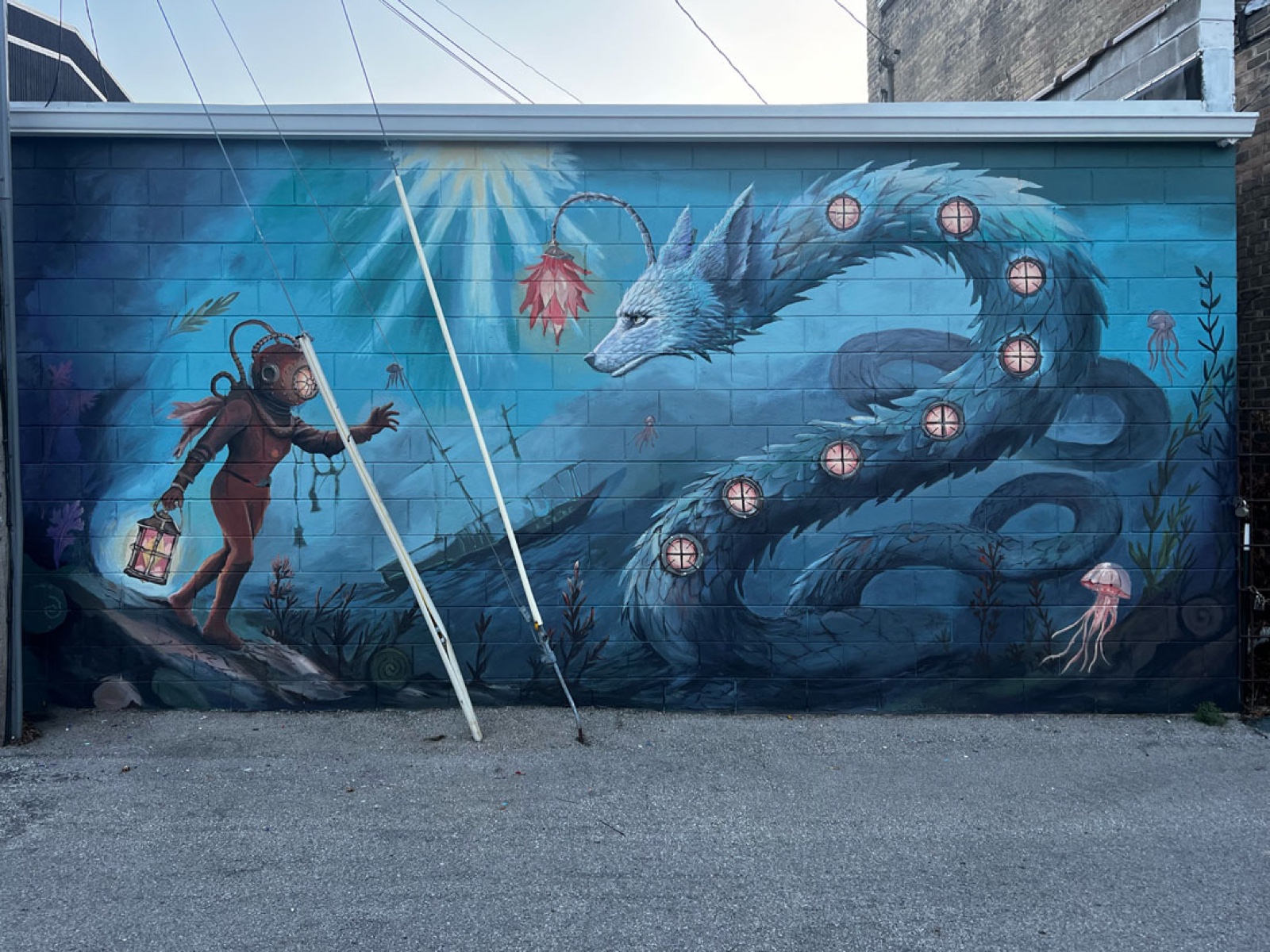 The Loodoo mural, Algoma: a lantern-bearing diver in an antique dive suit meets a serpentine white water-wolf coiling through blue water above a drowned shipwreck, portholes glowing along its body.